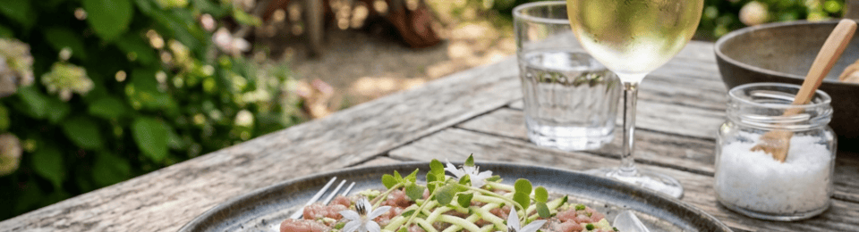 Tuna tartare and diced cucumber dish on a plate beside wine in a garden